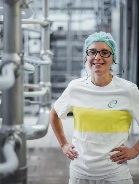 Une femme qui sourit, elle debout dans une usine